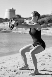 Woman doing a loaded squat with a disk in an Ibiza beach.